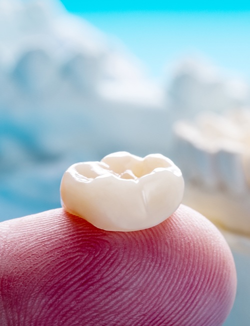 Dental crown restoration resting on fingertip