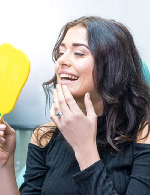 woman admiring her smile in a mirror after getting a dental crown