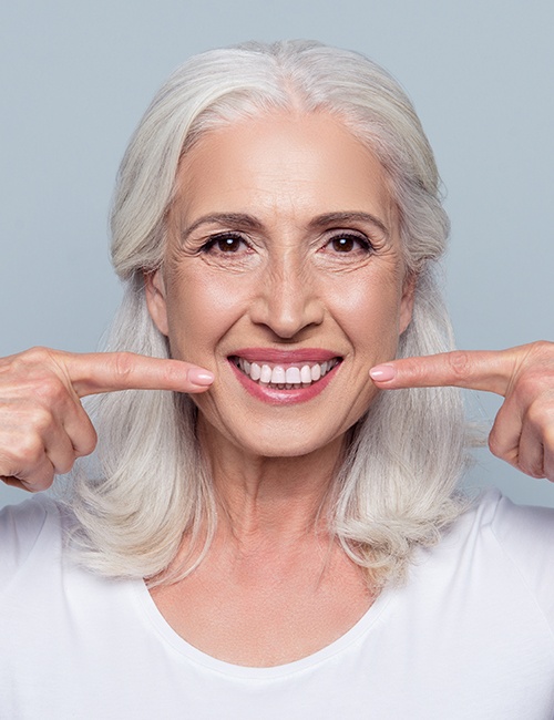 Woman with dentures pointing to her smile