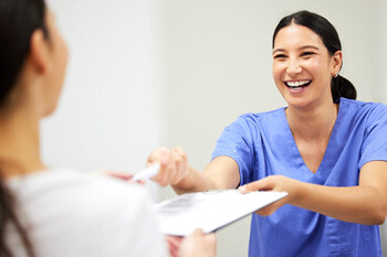 dental assistant smiling while handing patient form