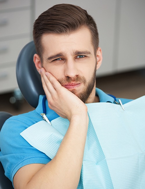 Man in dental chair holding cheek before tooth extraction