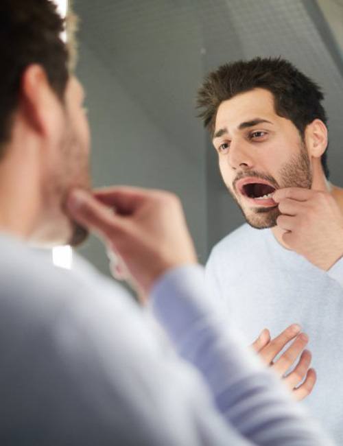 Man pulling his lip back to check his teeth in mirror