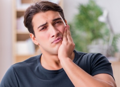 Man in need of emergency dentistry holding cheek in pain