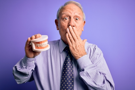 older man holding dentures in hand