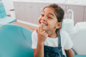 Young girl in dentist’s chair pointing to her tooth