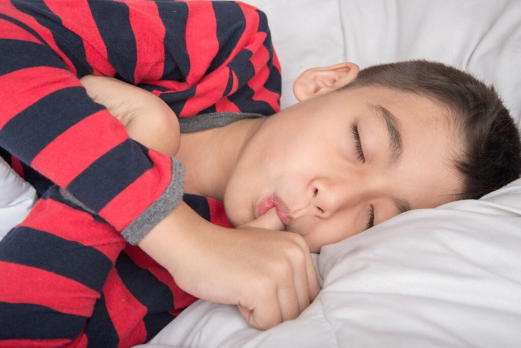 Boy in striped shirt laying down with eyes closed sucking thumb