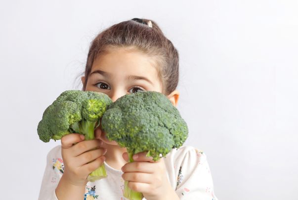 A little girl holding broccoli